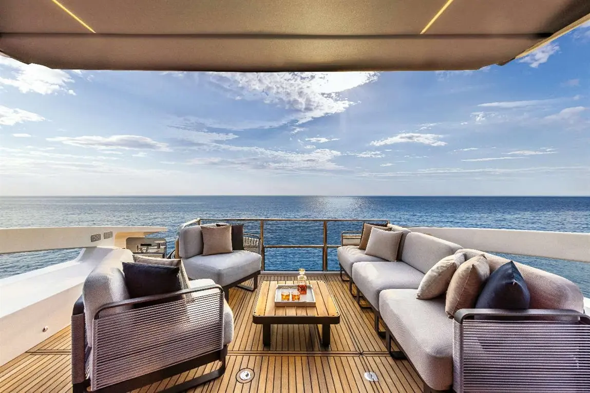 Stylish patio with grey sofas and a wooden table overlooking the ocean, under a shaded canopy. Perfect for relaxation.